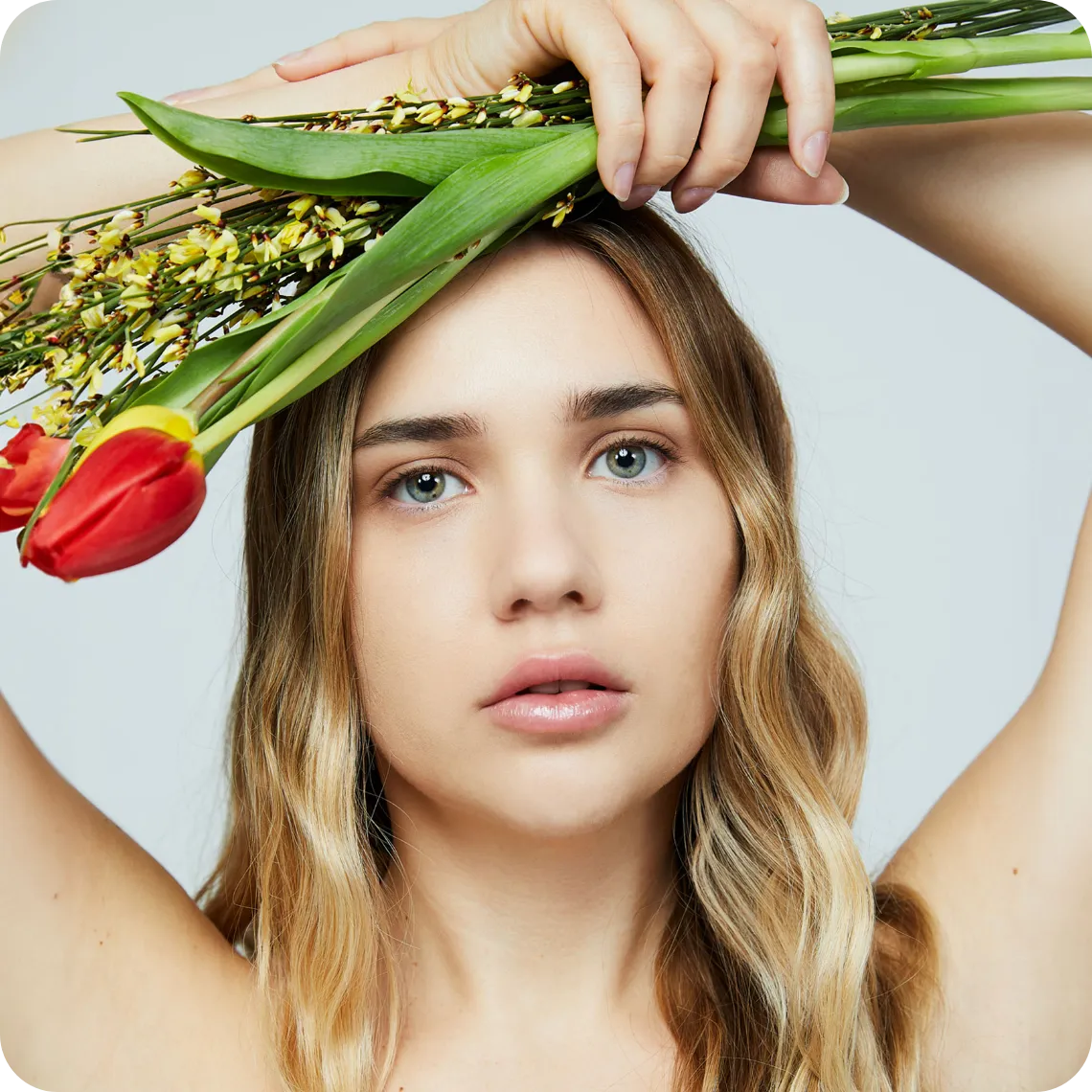 Foto di copertina del wikiglossario relativo agli interventi di chirurgia estetica e ai trattamenti di medicina estetica in cui è presente una modella con occhi verdi e capelli biondi che tiene in mano, posti sopra la testa, dei fiori.