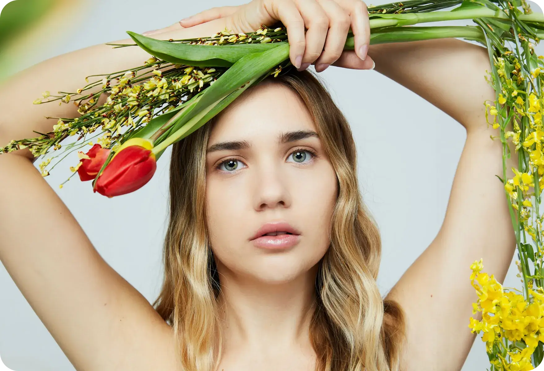 Foto di copertina del wikiglossario relativo agli interventi di chirurgia estetica e ai trattamenti di medicina estetica in cui è presente una modella con occhi verdi e capelli biondi che tiene in mano, posti sopra la testa, dei fiori.